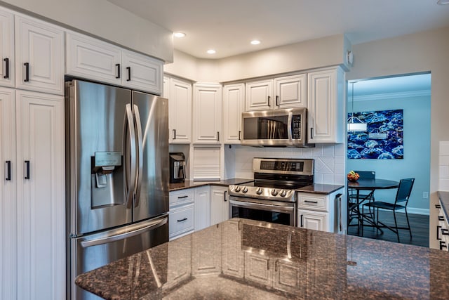 kitchen with white cabinets, appliances with stainless steel finishes, decorative backsplash, and dark stone countertops