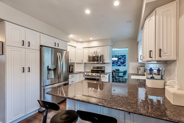 kitchen featuring appliances with stainless steel finishes, dark wood-style flooring, a peninsula, a sink, and backsplash