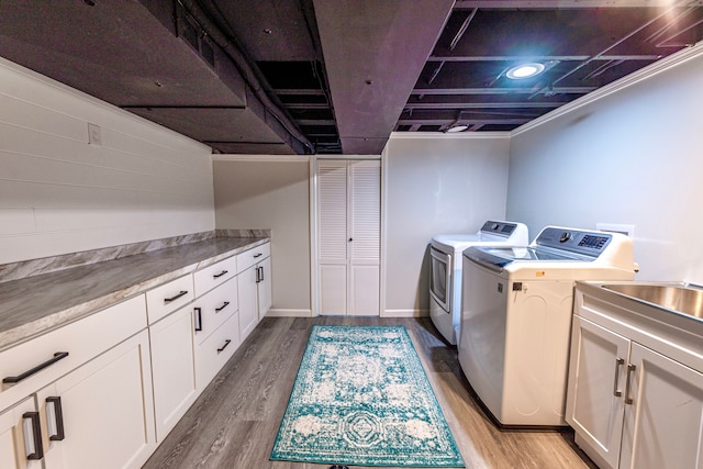 washroom featuring separate washer and dryer, cabinet space, and light wood-style flooring