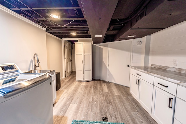 clothes washing area featuring light wood-type flooring, washer / dryer, a sink, and cabinet space