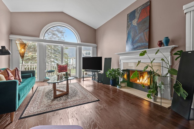 living area with vaulted ceiling, a tiled fireplace, and wood finished floors