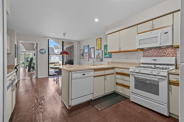 kitchen with a peninsula, white appliances, light countertops, and dark wood-type flooring