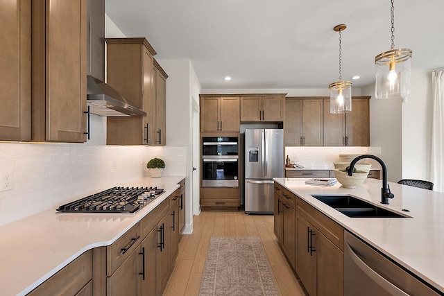 kitchen with decorative light fixtures, light countertops, light wood-style flooring, appliances with stainless steel finishes, and a sink