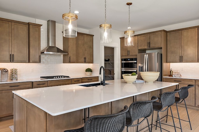 kitchen with a sink, a kitchen breakfast bar, stainless steel appliances, wall chimney exhaust hood, and light wood finished floors