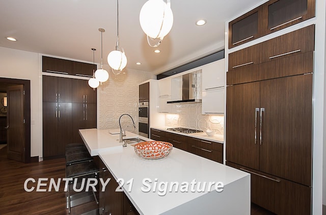 kitchen with dark brown cabinetry, wall chimney exhaust hood, stainless steel appliances, light countertops, and a sink