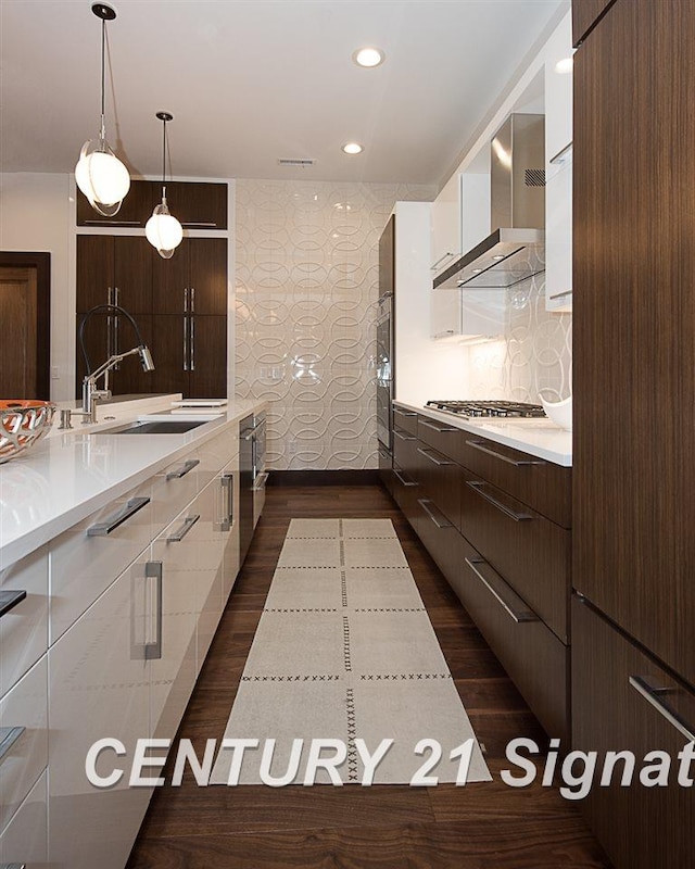 kitchen featuring white cabinets, modern cabinets, wall chimney range hood, stainless steel gas stovetop, and a sink