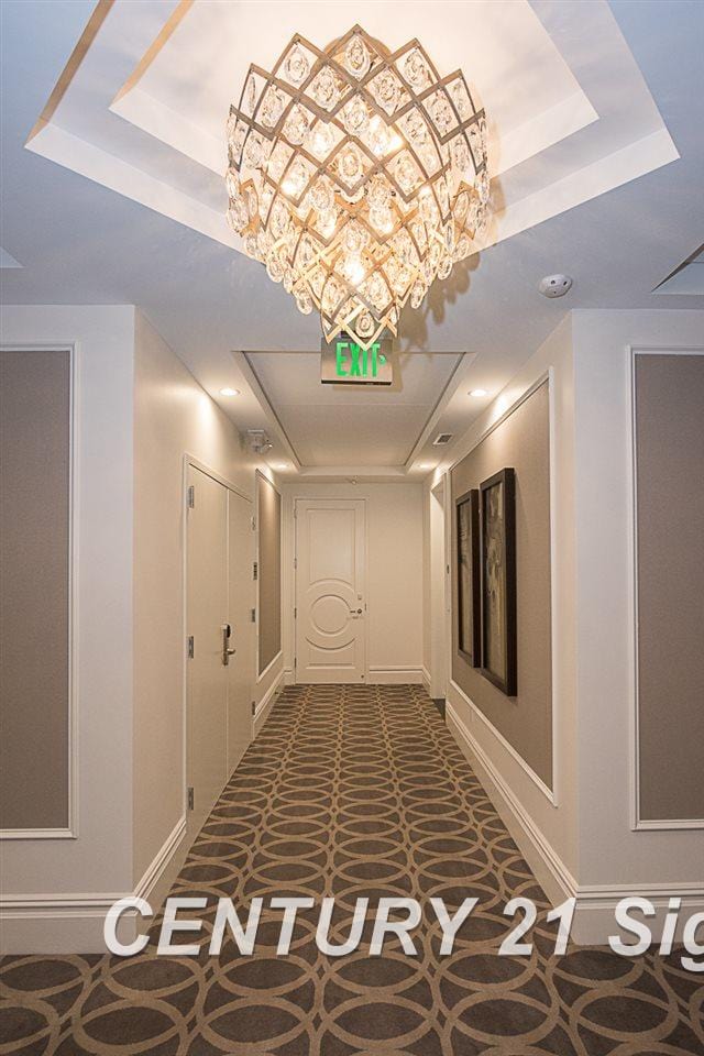 hallway with carpet, a raised ceiling, and baseboards