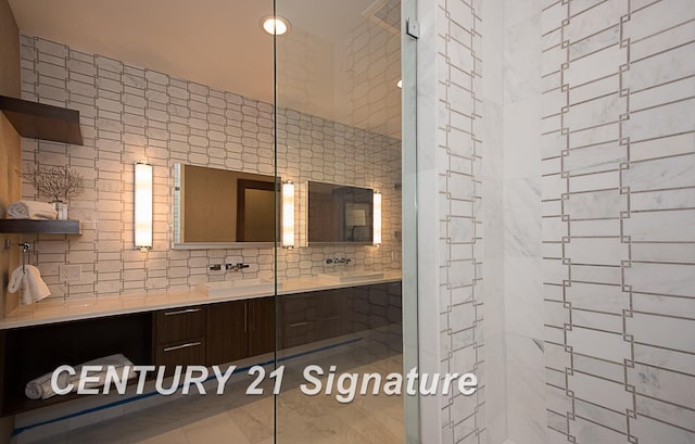 full bath featuring a tile shower, a sink, tile walls, and double vanity