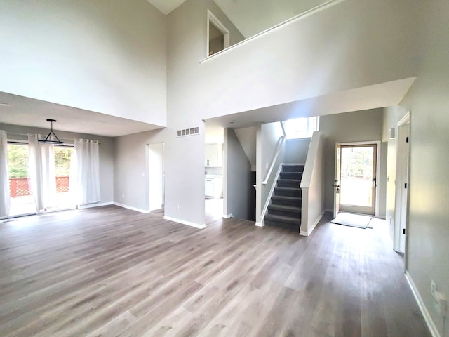 unfurnished living room featuring wood finished floors, visible vents, baseboards, stairs, and a towering ceiling