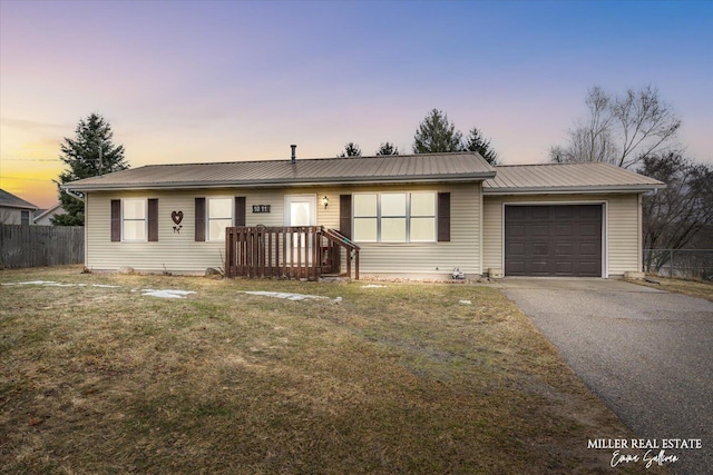 ranch-style house with aphalt driveway, metal roof, an attached garage, fence, and a yard