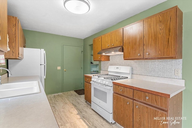 kitchen with tasteful backsplash, white range with gas cooktop, light countertops, under cabinet range hood, and a sink