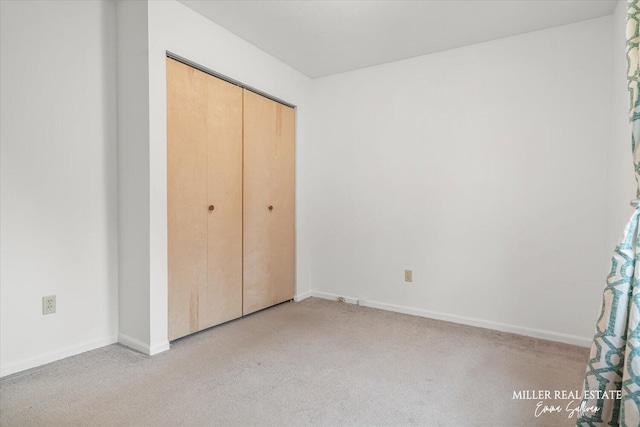 unfurnished bedroom with light carpet, baseboards, and a closet