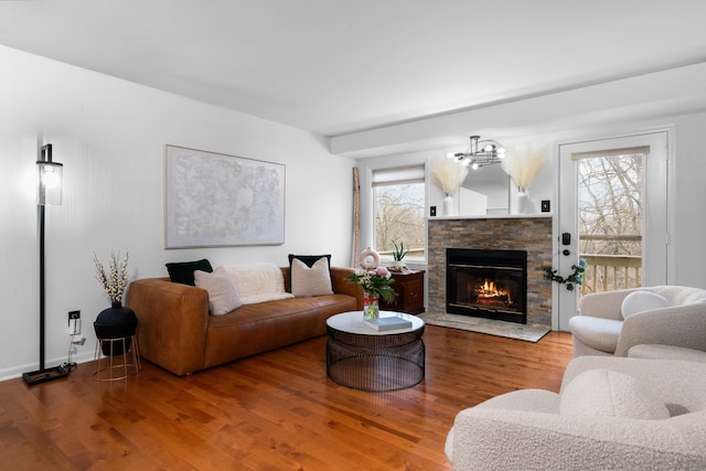 living room featuring a notable chandelier, a fireplace, baseboards, and wood finished floors