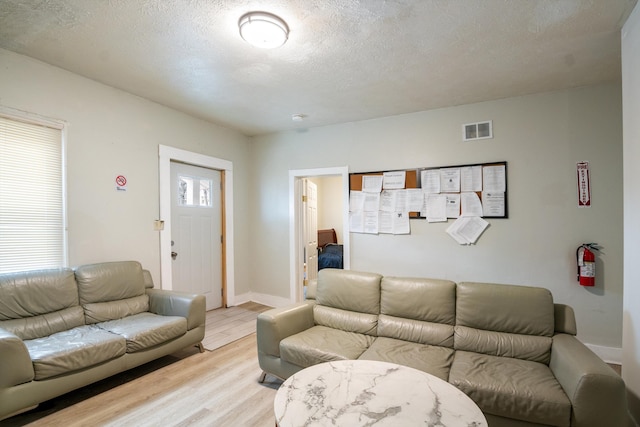 living room featuring a textured ceiling, light wood finished floors, visible vents, and baseboards