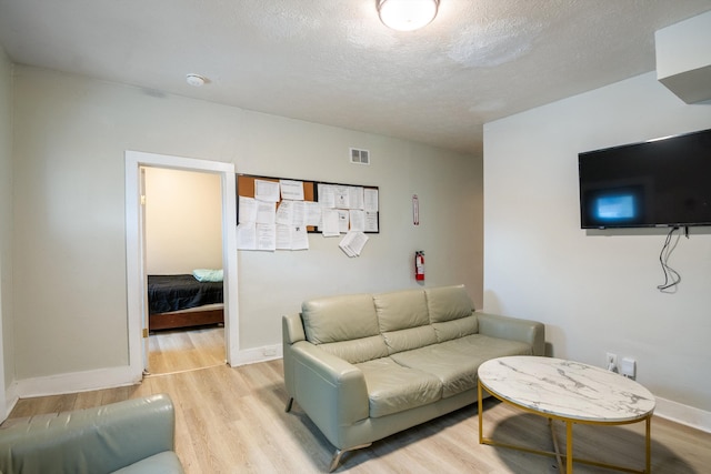 living room featuring light wood-type flooring, visible vents, a textured ceiling, and baseboards