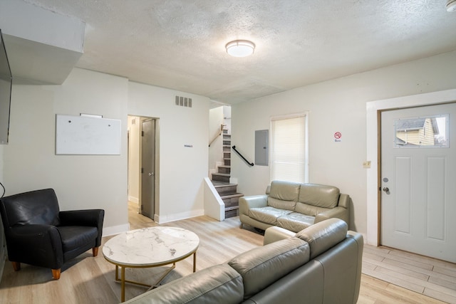 living area featuring visible vents, light wood-style flooring, stairway, a textured ceiling, and electric panel