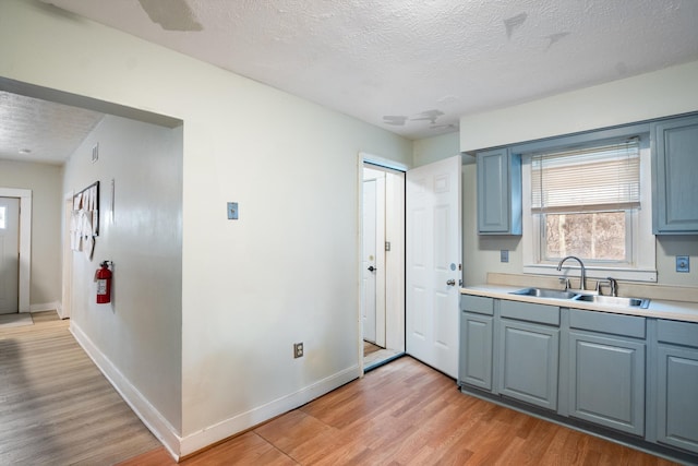 kitchen featuring light countertops, light wood-type flooring, a sink, and baseboards