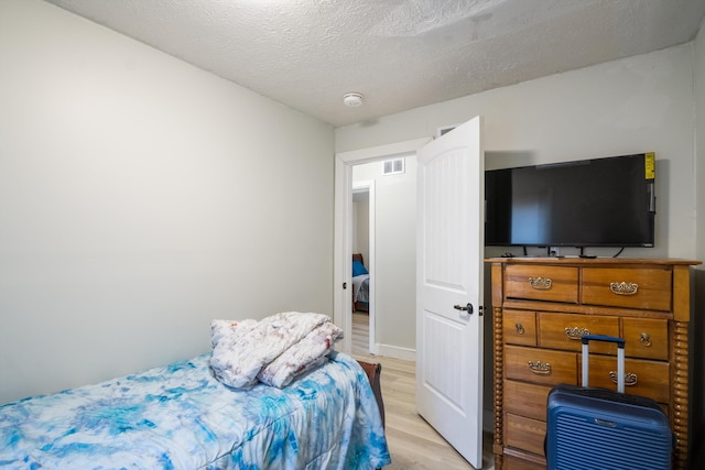 bedroom with light wood-type flooring, visible vents, and a textured ceiling