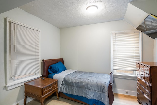 bedroom with vaulted ceiling, a textured ceiling, baseboards, and light wood-style floors