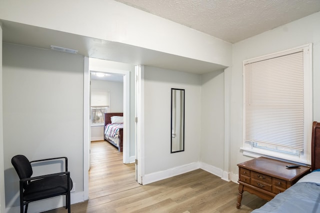 bedroom with baseboards, visible vents, light wood-style flooring, and a textured ceiling