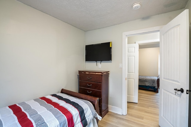 bedroom with baseboards, a textured ceiling, and light wood finished floors