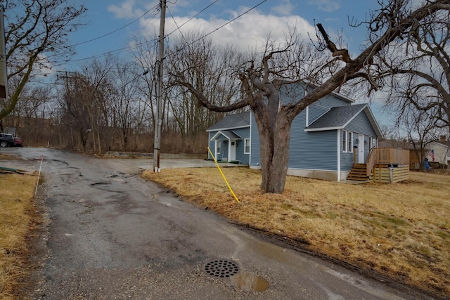 view of front of property with aphalt driveway, roof with shingles, and a front lawn