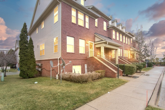 property exterior at dusk with brick siding, a lawn, and stairs