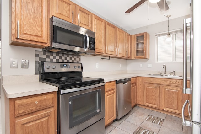 kitchen with pendant lighting, light countertops, appliances with stainless steel finishes, glass insert cabinets, and a sink