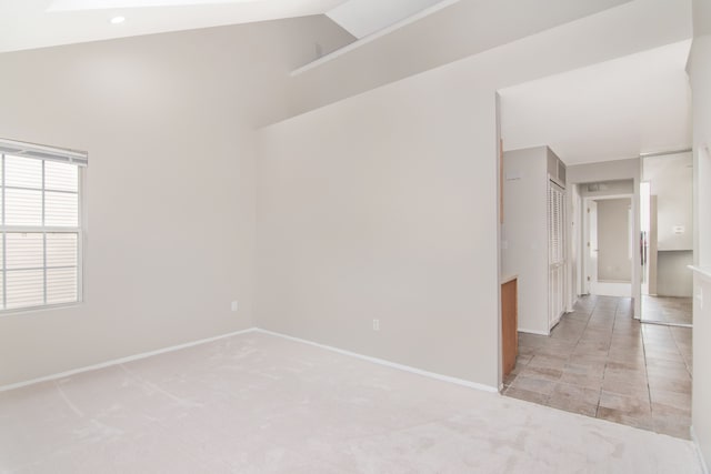 unfurnished room with light tile patterned flooring, baseboards, vaulted ceiling, and light colored carpet