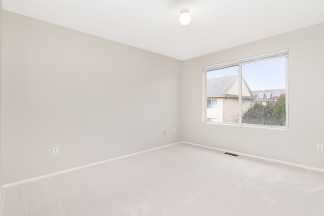 empty room featuring light carpet, visible vents, and baseboards