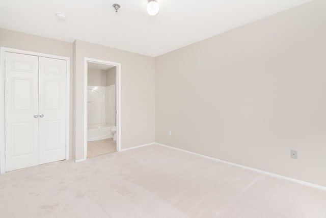 unfurnished bedroom featuring a closet, light colored carpet, ensuite bath, and baseboards