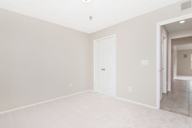 unfurnished bedroom featuring baseboards, visible vents, a closet, and light colored carpet