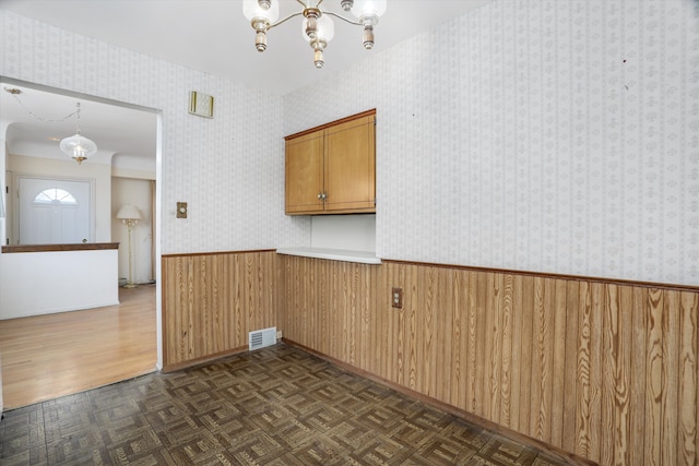 unfurnished room with a wainscoted wall, visible vents, wallpapered walls, an inviting chandelier, and parquet flooring