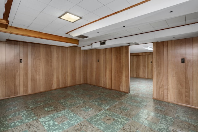 finished below grade area featuring wooden walls, visible vents, and tile patterned floors