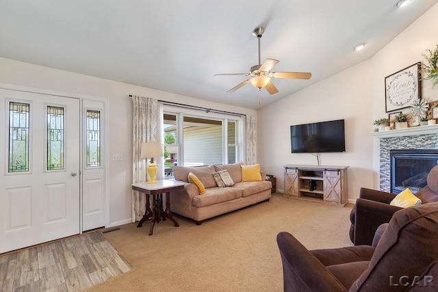 living area with lofted ceiling, light carpet, ceiling fan, and a tiled fireplace