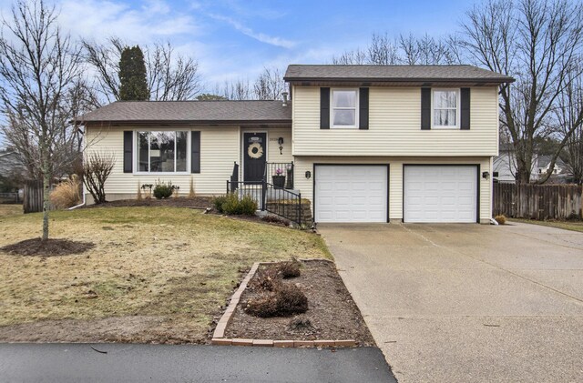 split level home featuring an attached garage, a shingled roof, fence, driveway, and a front yard