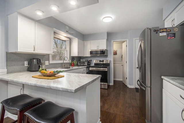 kitchen with dark wood-style flooring, appliances with stainless steel finishes, white cabinetry, a sink, and a peninsula