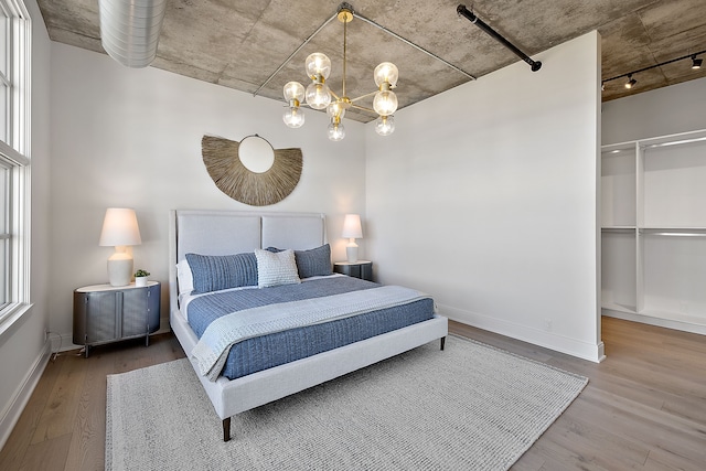 bedroom featuring a walk in closet, a notable chandelier, baseboards, and wood finished floors