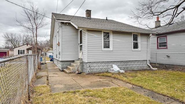 back of house with entry steps, a fenced backyard, a chimney, and a shingled roof