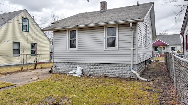 back of house with roof with shingles, a chimney, a fenced backyard, and a lawn