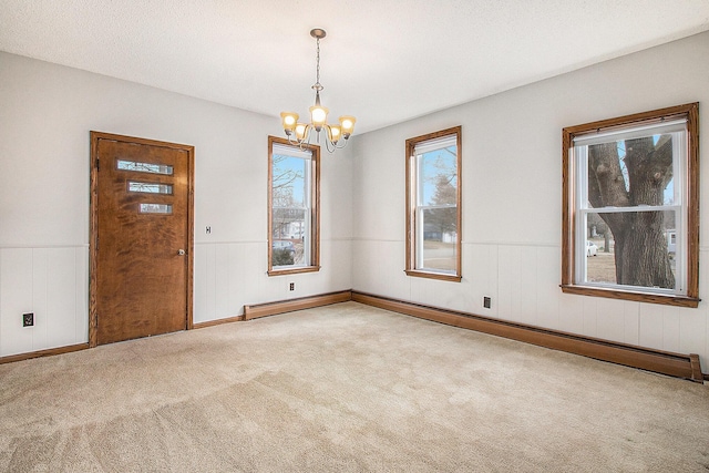 carpeted spare room featuring an inviting chandelier, a baseboard heating unit, and wainscoting