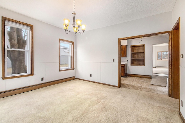 empty room with a textured ceiling, a notable chandelier, a baseboard heating unit, light carpet, and wainscoting