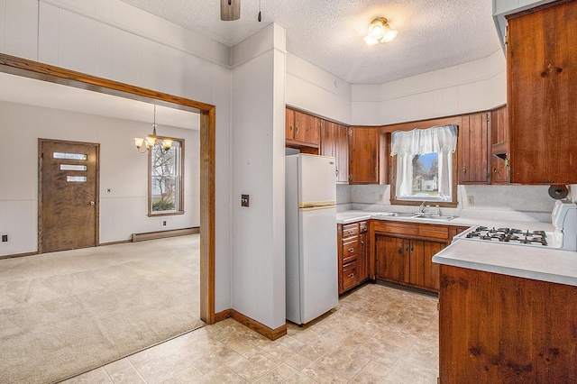 kitchen featuring brown cabinets, a baseboard radiator, light colored carpet, freestanding refrigerator, and a sink