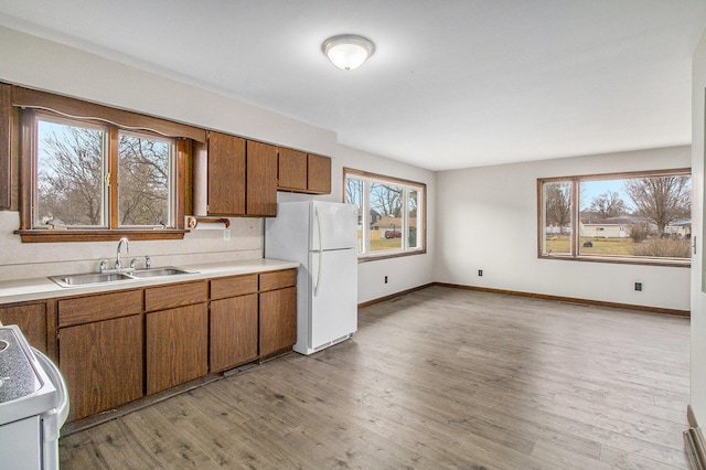 kitchen featuring brown cabinetry, freestanding refrigerator, range, and a sink