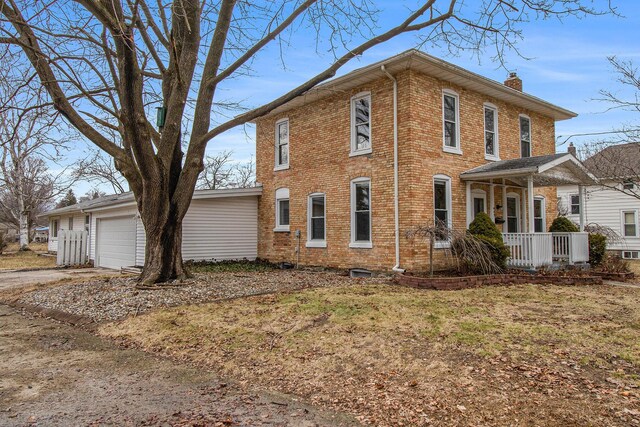 view of side of home with driveway, a chimney, an attached garage, a porch, and brick siding