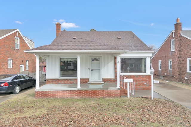 bungalow featuring a shingled roof, concrete driveway, a chimney, covered porch, and brick siding