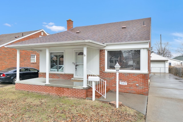 view of front of house with brick siding, a chimney, a shingled roof, a porch, and a garage