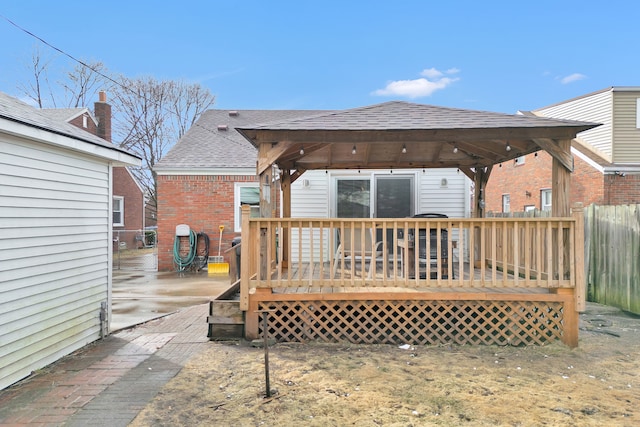 rear view of property with roof with shingles, fence, a wooden deck, and brick siding