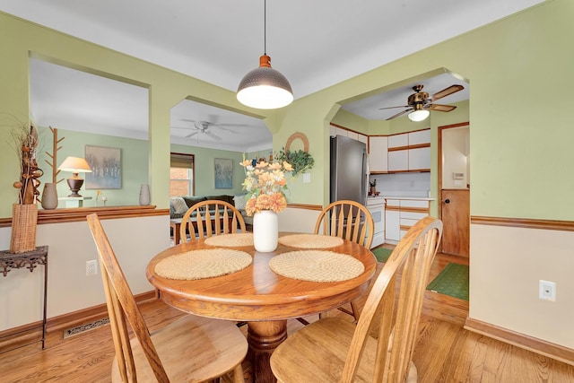 dining area with light wood finished floors, baseboards, visible vents, and arched walkways