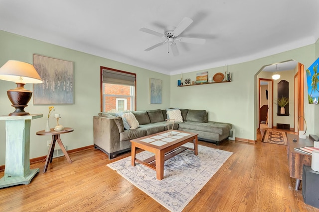 living room featuring arched walkways, ceiling fan, wood finished floors, and baseboards